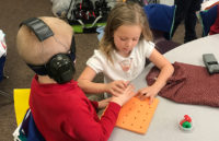 A young student guides her deaf-blind classmate.